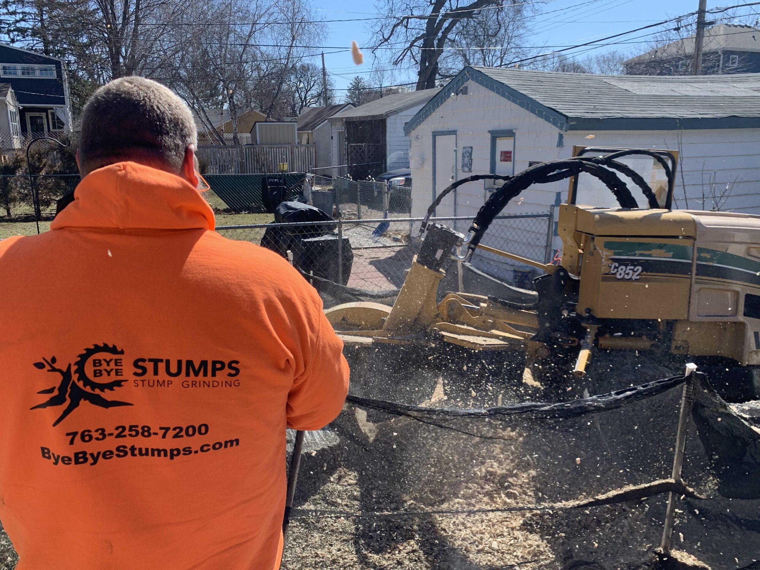 man watching a machine grind down a tree stump - tree stump removal machine